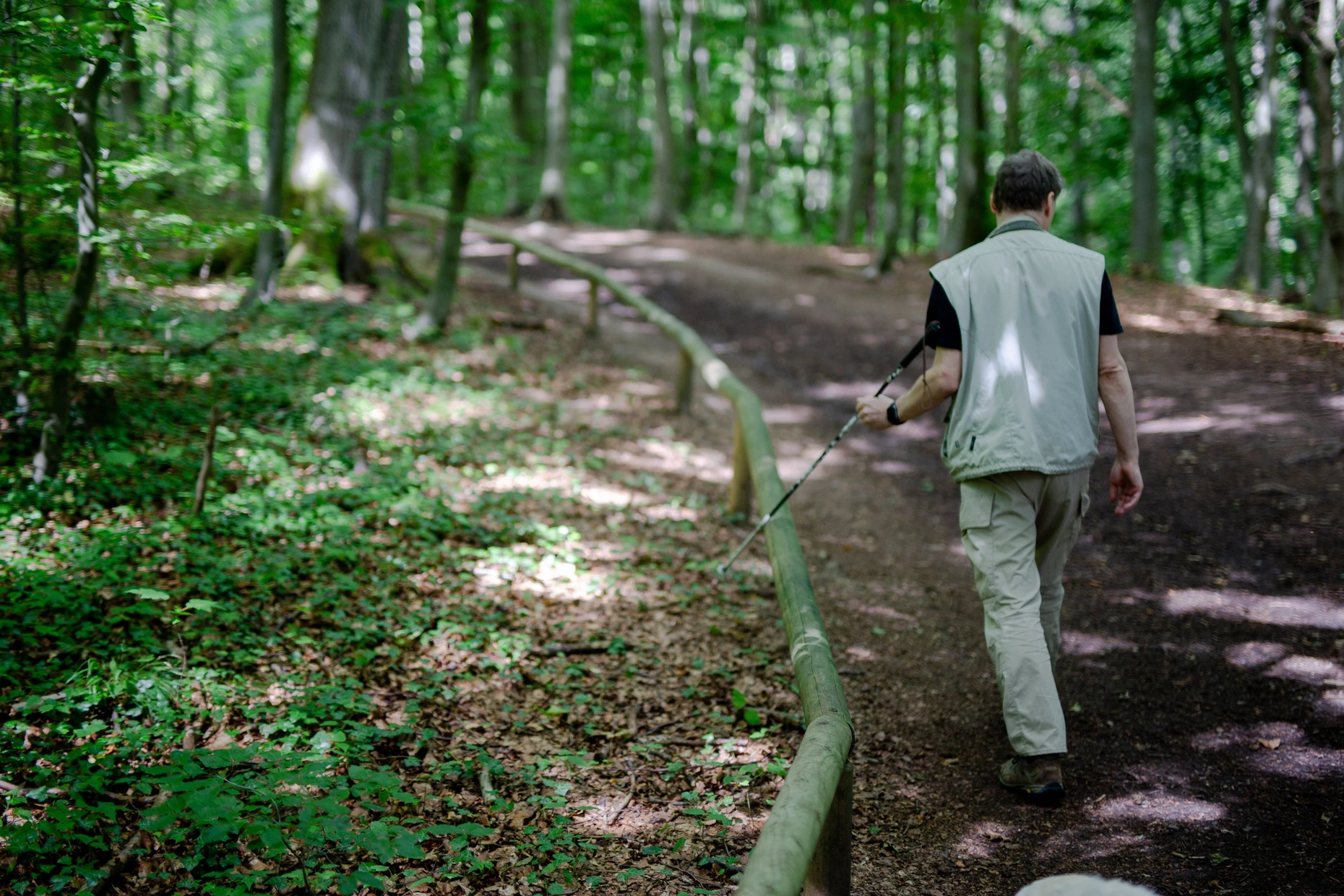 Ein Mann fährt mit seinem Blindenstock über das Holzgeländer des Blindenwanderweges am Stadtrand von Kassel.
