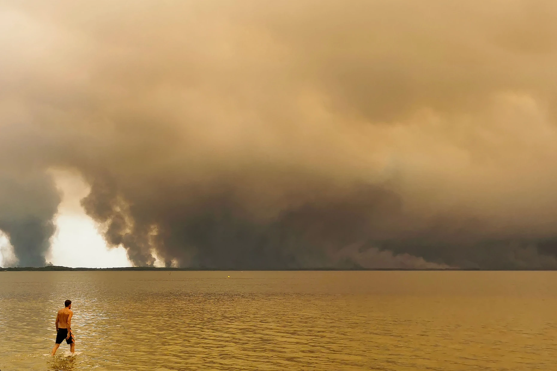 Ein Strandbesucher spaziert am Strand von Moutchic in Lacanau im Südwesten Frankreichs am Etang de Lacanau entlang, während Rauchwolken von einem Waldbrand in den Himmel aufsteigen.