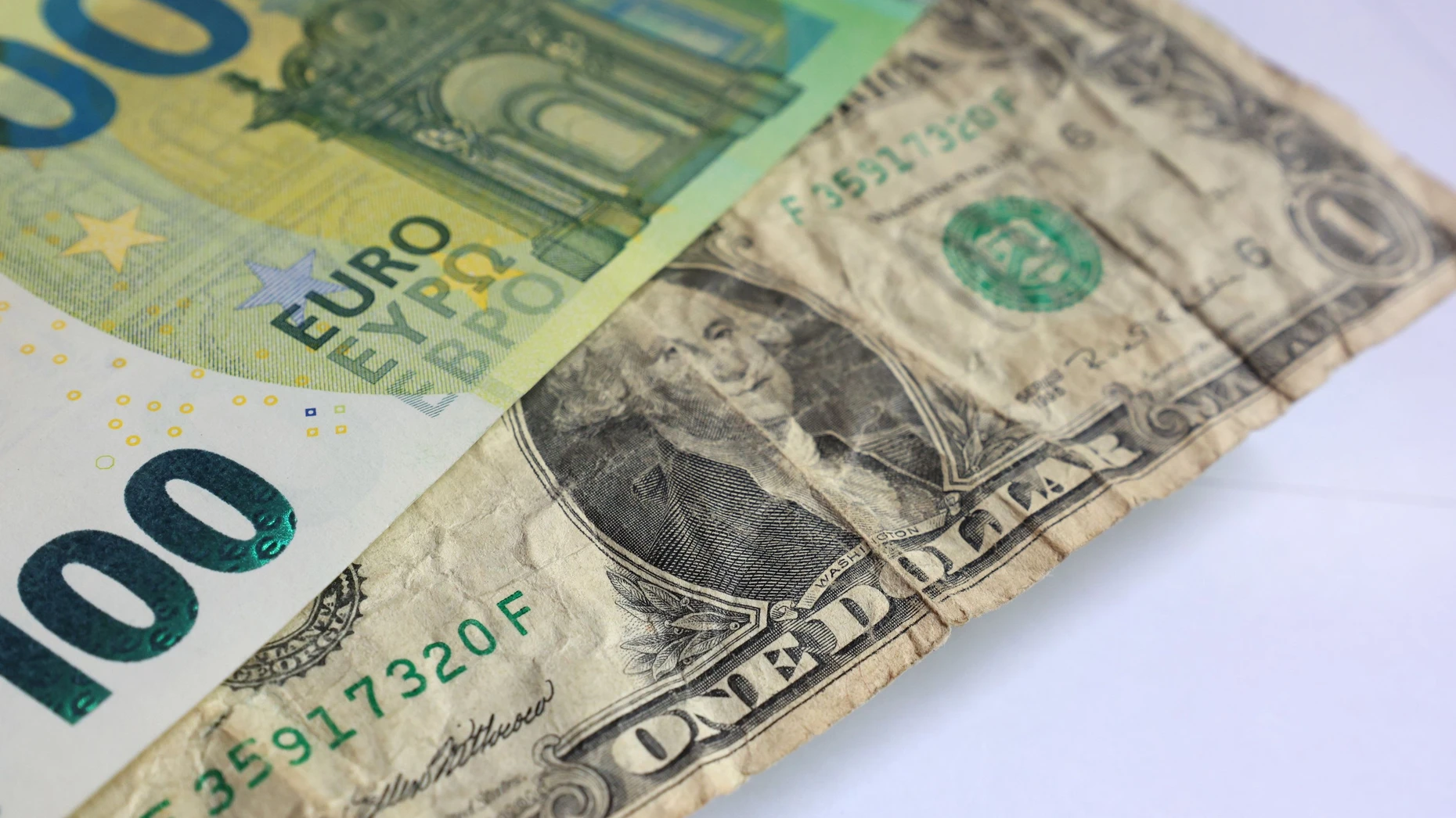 Gebrauchsspuren: Ein US-Dollar liegt unter einer 100-Euro-Banknote.