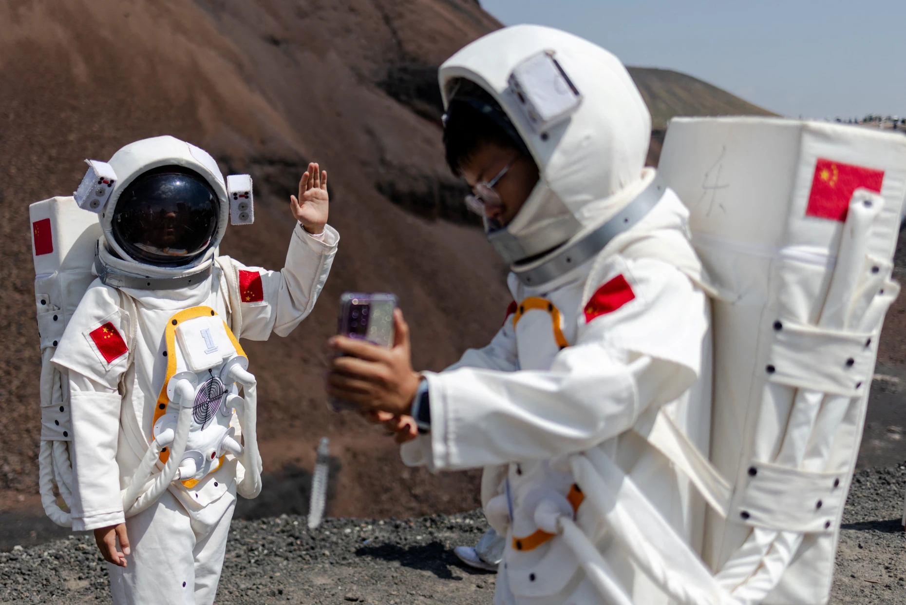 Die perfekte Foto-Opportunity: Besucher in Raumanzügen fotografieren sich mit dem Smartphone vor der Vulkanlandschaft.