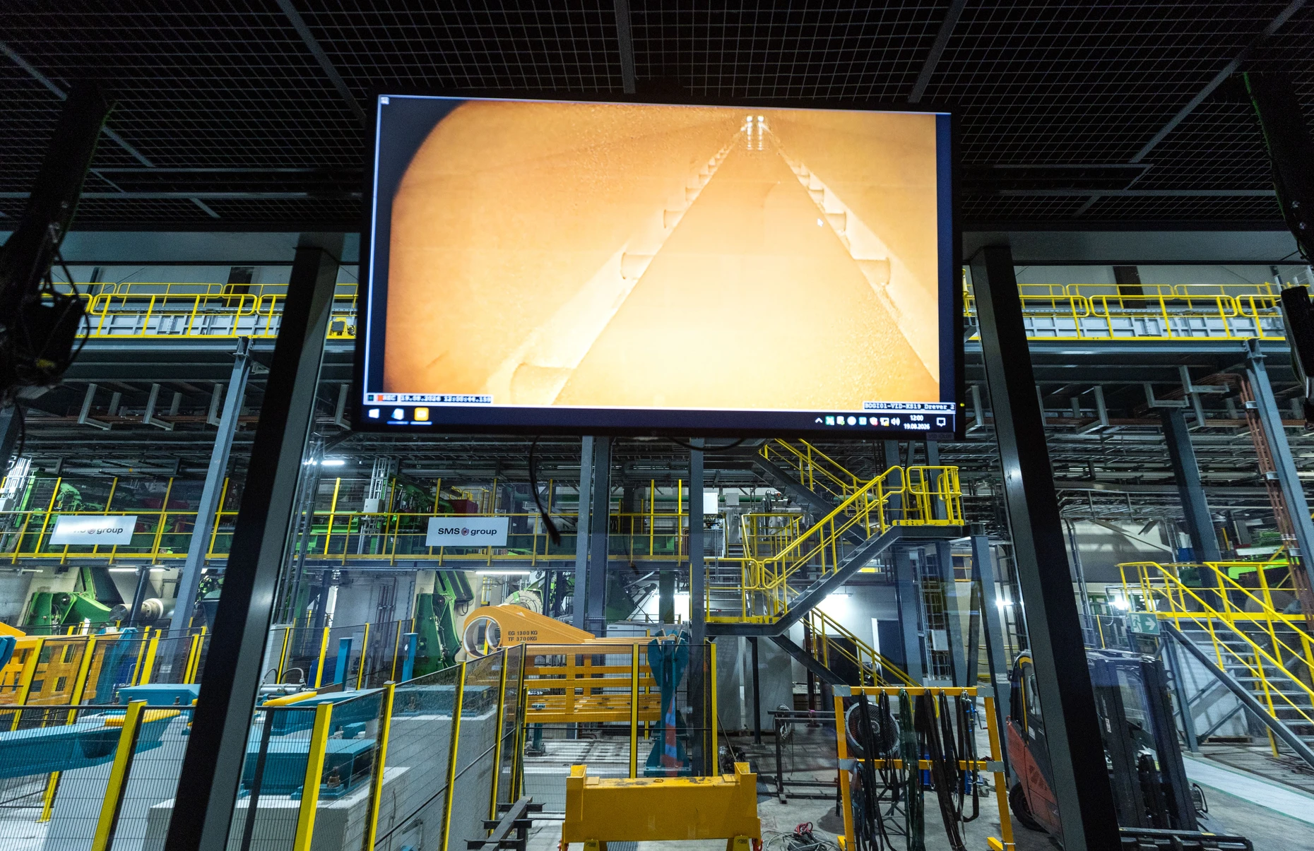 Langgezogener Ofen von außen und von innen: Blick in die Halle des Bochumer Thyssenkruppwerks vom Leitstand aus und auf einem Bildschirm der Blick ins Innere des Ofens