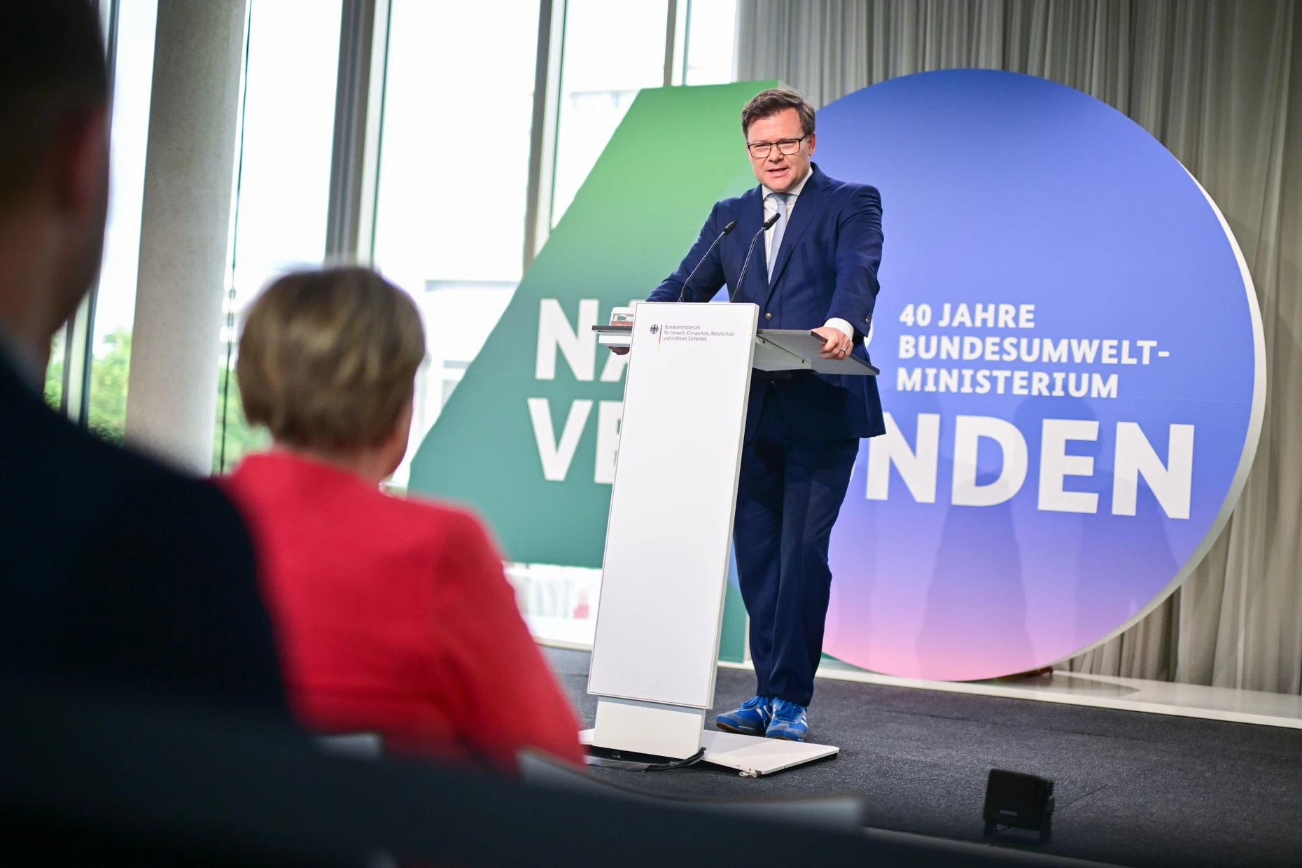Carsten Schneider (SPD) hält zum 40. Geburtstag seines Ministeriums eine Rede, der auch die frühere Umweltministerin Angela Merkel (CDU) zuhört.