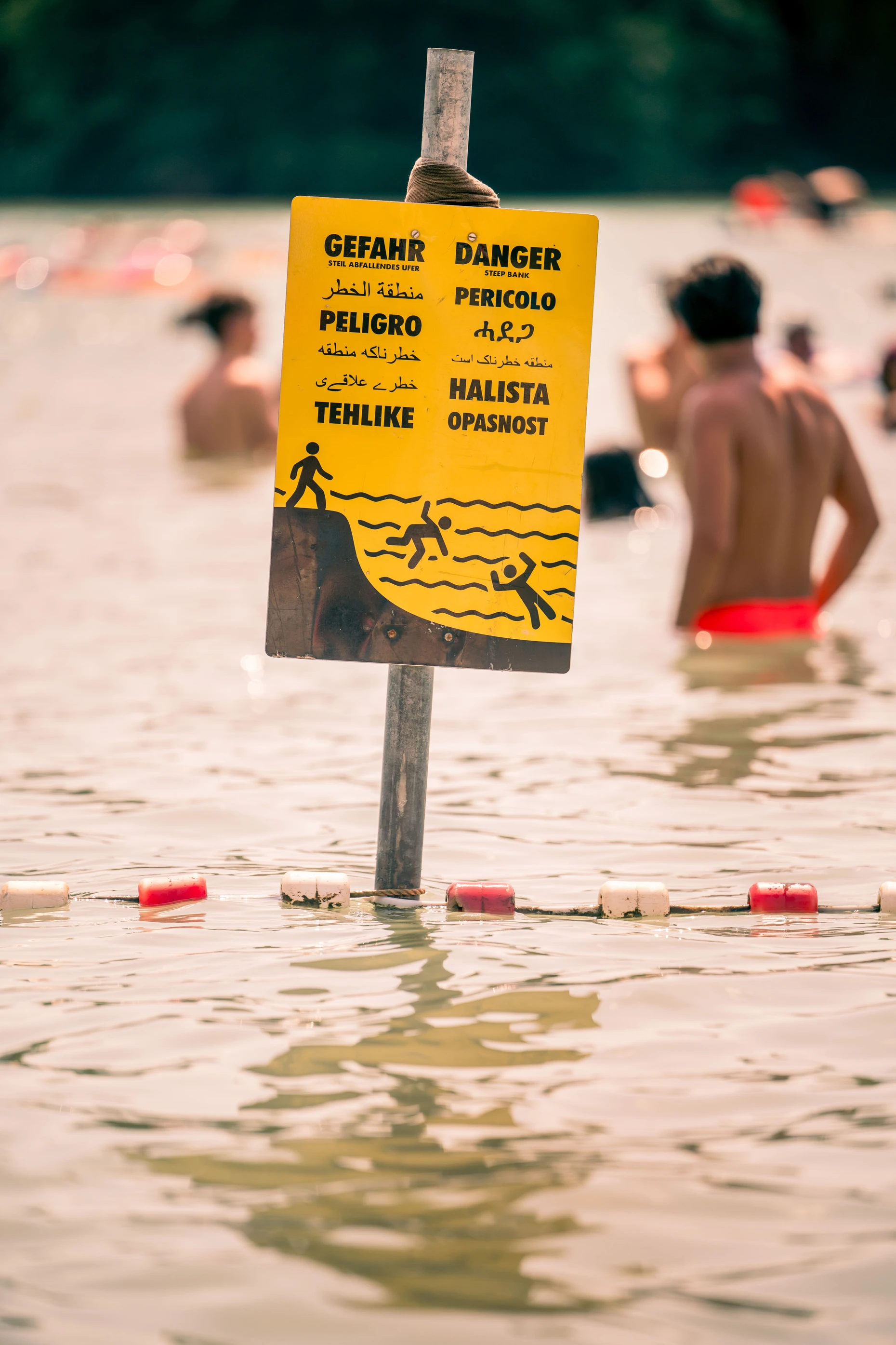 Ein Schild warnt in mehreren Sprachen davor, dass der Grund des Sees plötzlich steil abfällt.
