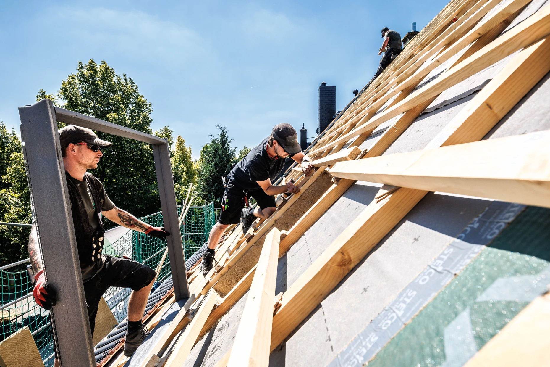 Arbeit bei praller Sonne: Dachdecker montieren auf einem Dach den Rahmen für ein Fenster.