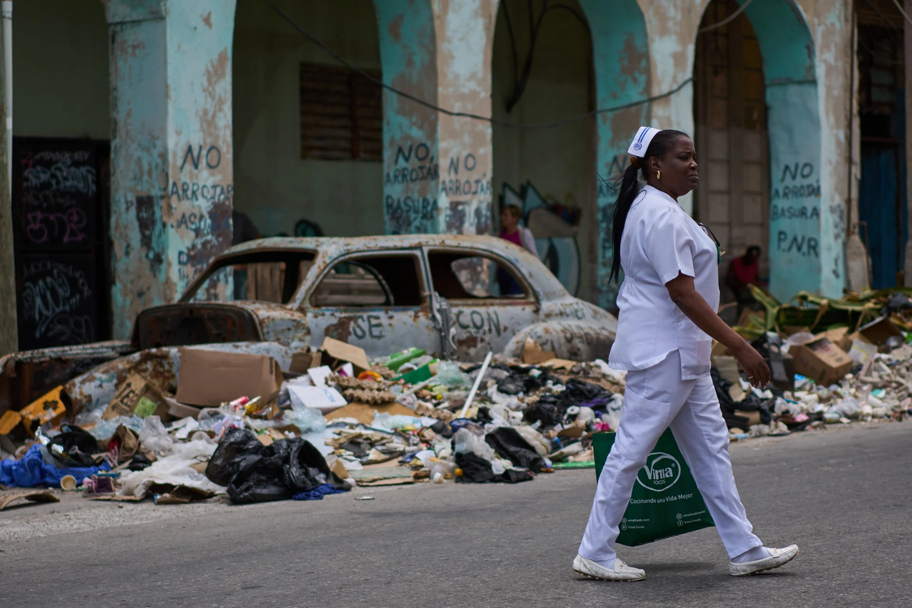 Eine Krankenschwester geht im April auf einer Straße in Havanna an Müll und einem verlassenen amerikanischen Oldtimer vorbei.