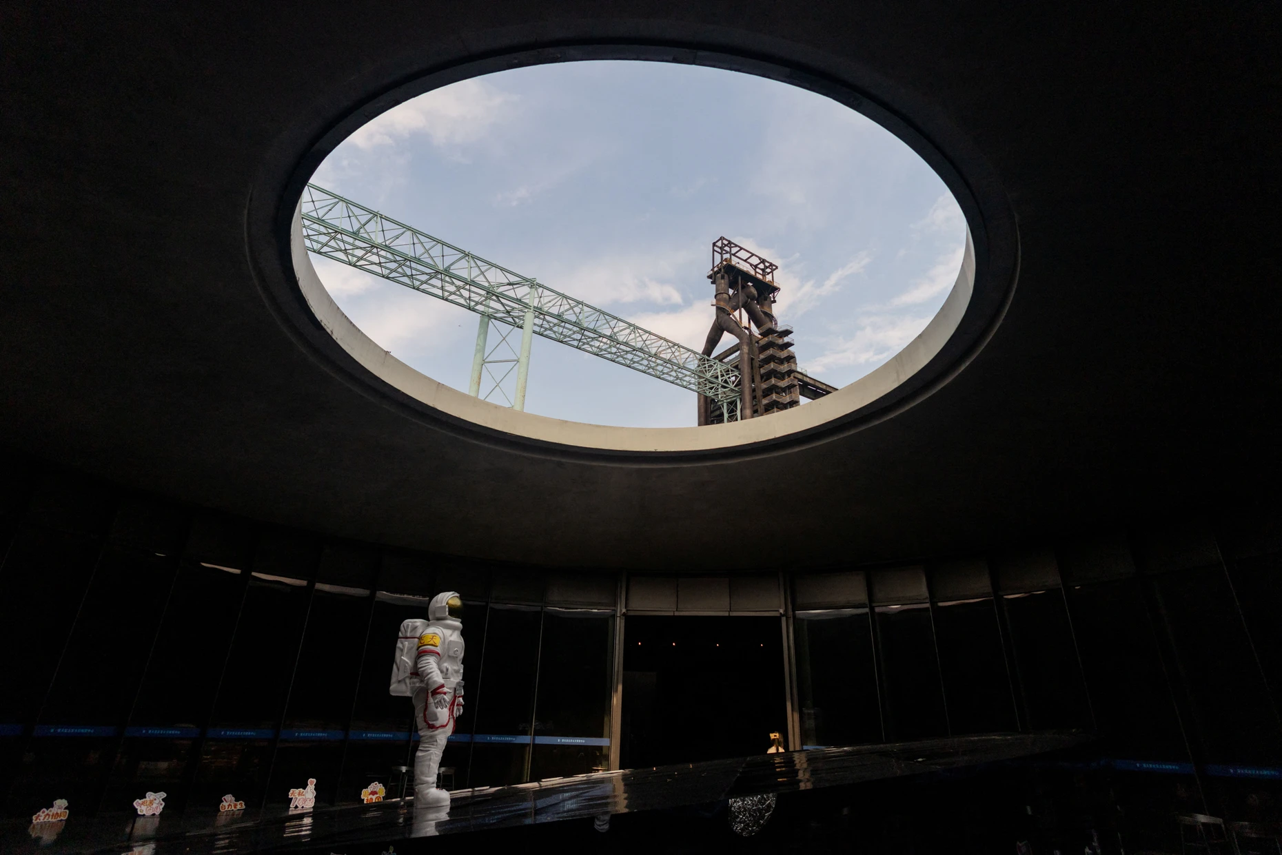 Eine Astronautenfigur steht unter der runden Dachöffnung des Shou-Wang-Tian-Gong Beijing Space Exploration Center im Shougang-Park in Peking