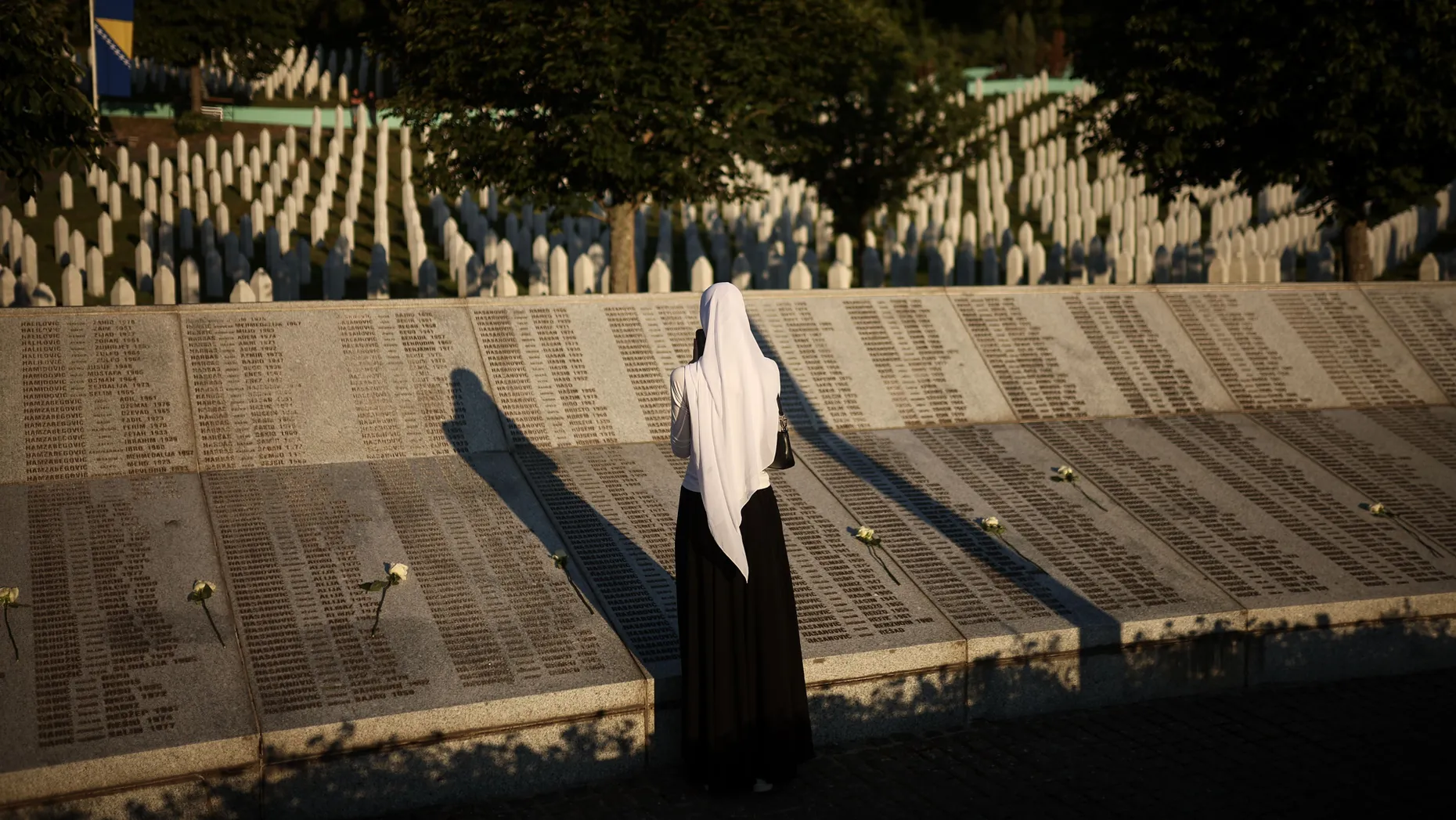 Eine Frau steht neben dem Denkmal mit den Namen der Opfer des Völkermords von Srebrenica im Gedenkzentrum Srebrenica in Potočari, Bosnien.