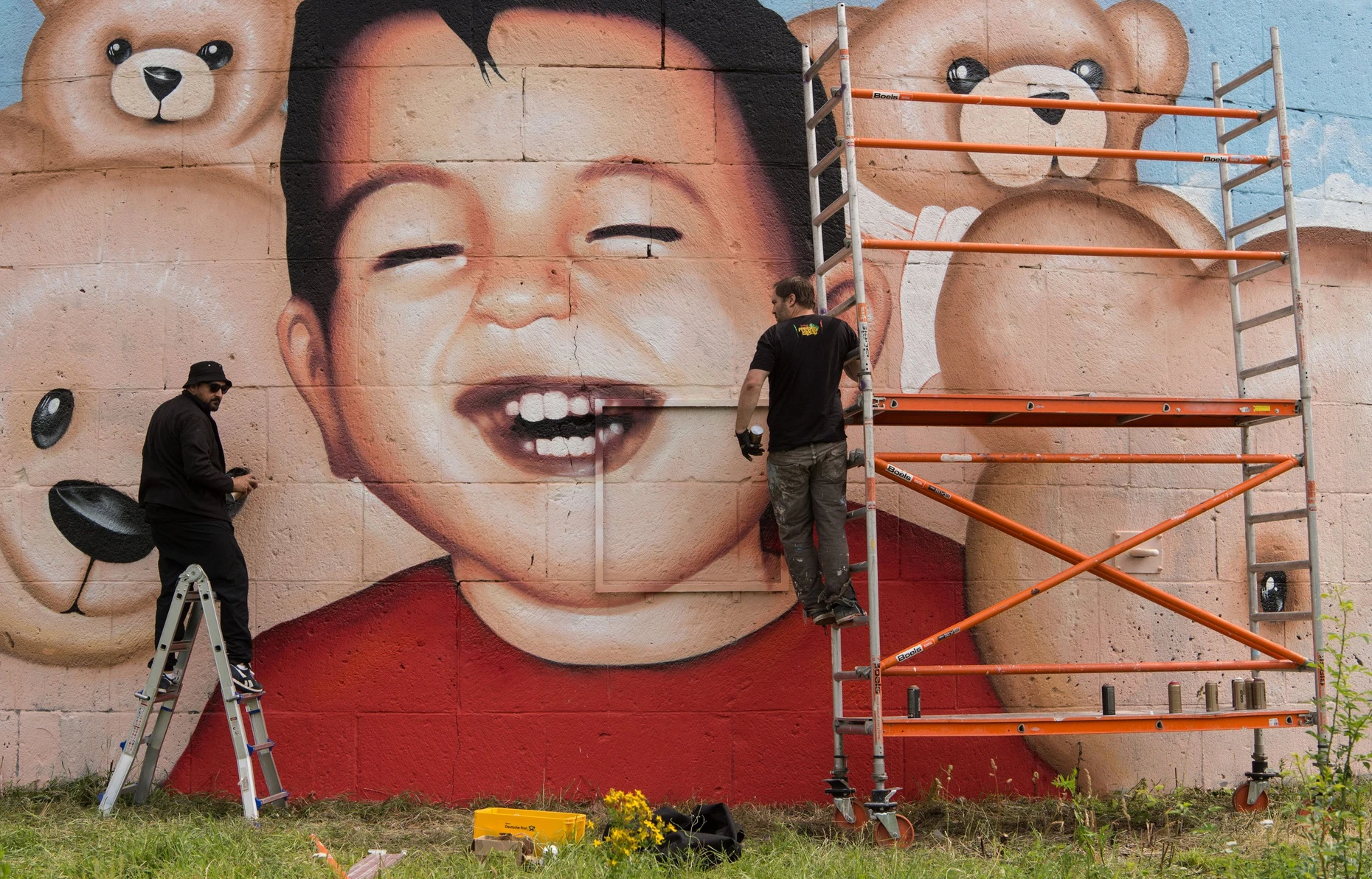 Nachdem das alte Bild, die Reproduktion des Fotos von Kurdi, zerstört wurde, entstand das neue Motiv - der lachende Junge, inmitten von Teddys. Das Bild löste Kontroversen über Kitsch und Kunst aus: Die Künstler Oğuz Şen (links) und Justus Becker im Jahr 2016