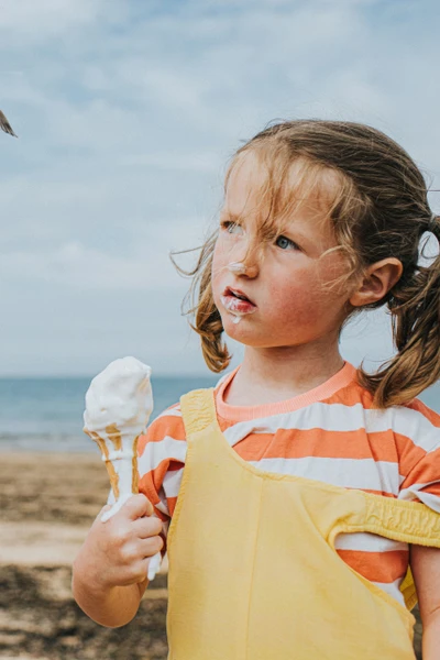 Zwei Kinder, ein Junge und ein Mädchen, stehen an einem Strand. In den Händen halten sie ein Eis, das bereits schmilzt.
