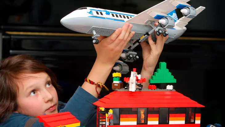 Ein Junge spielt mit einem Flugzeug und einem Haus aus Legosteinen.
