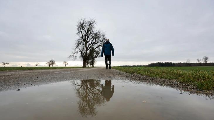 Baden-Württemberg, Biberach an der Riß: Ein Spaziergänger spiegelt sich in einer Regenpfütze.