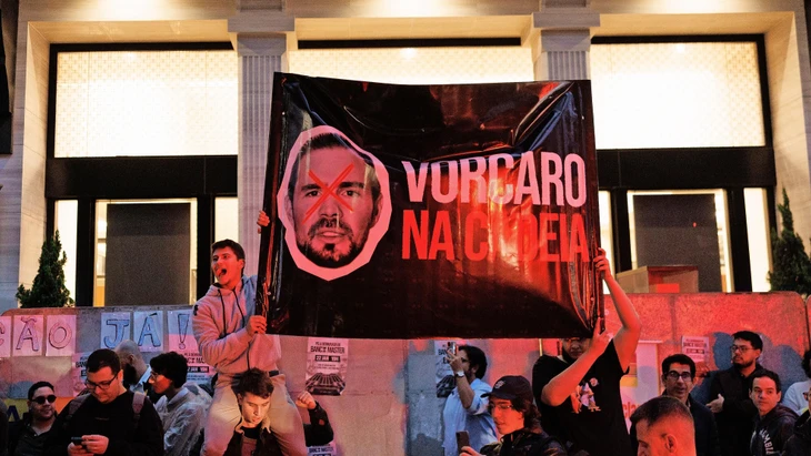 Aufgebrachte Kunden halten in São Paulo ein Plakat mit dem Gesicht des Bankers in die Höhe. Darauf fordern sie: „Vorcaro ins Gefängnis“.