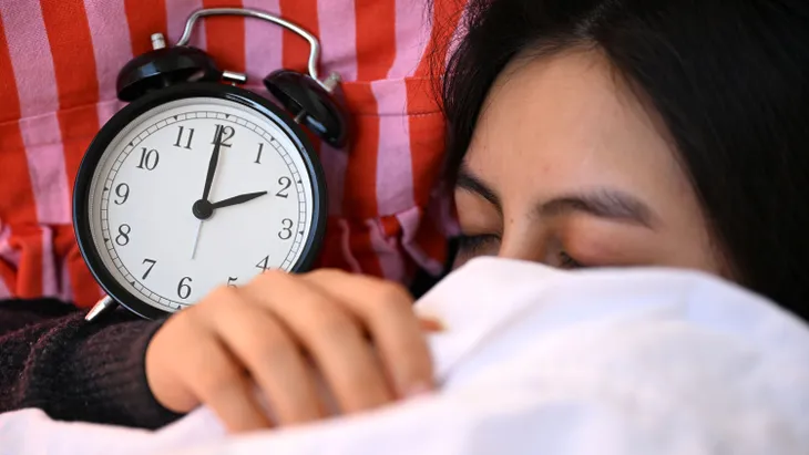 Eine schlafende Frau liegt mit einem Wecker im Bett.