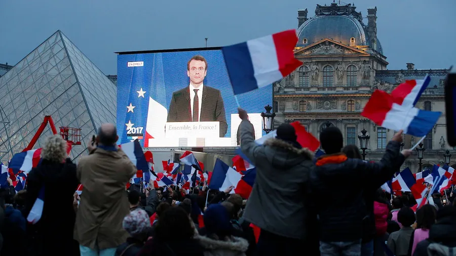 Macrons erste Ansprache nach der Wahl wird auf eine Leinwand vor dem Louvre übertragen, wo Tausende Fans ihn bejubeln.