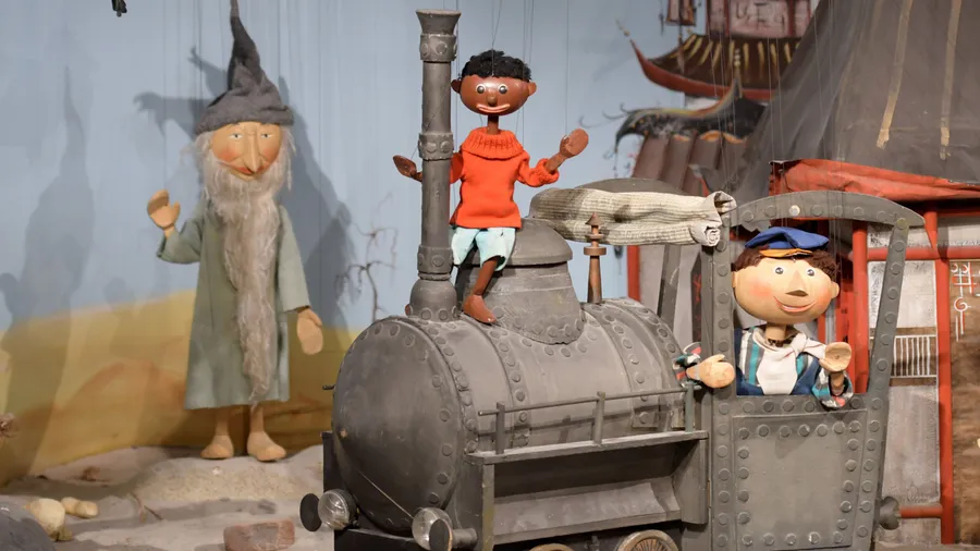 "Jim Knopf" und "Lukas" stehen zusammen mit der Lokomotive "Emma" im Puppentheatermuseum in Augsburg