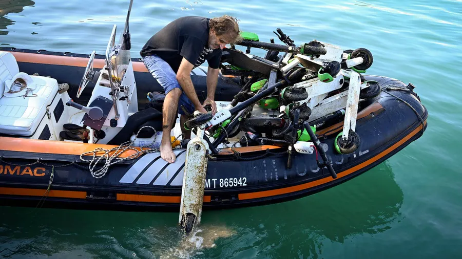 Ein Mann lädt einen Elektro-Roller auf ein Schlauchboot, während freiwillige Taucher an der Küste von Marseille aus dem Meerwasser bergen.