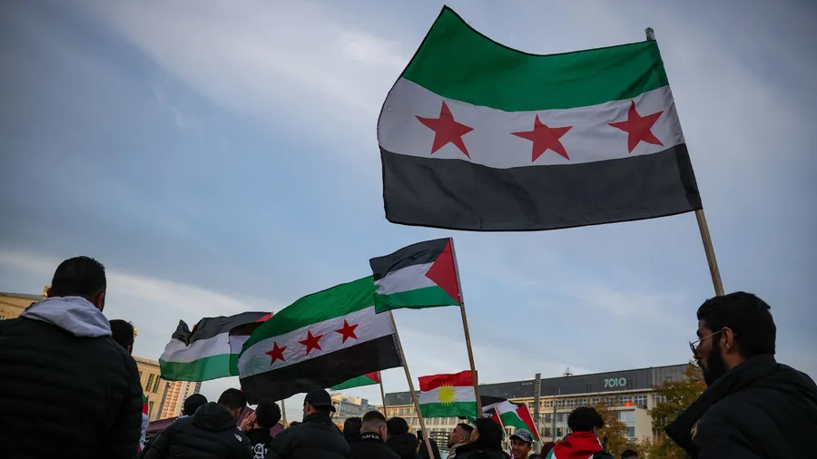 Teilnehmer einer Pro-Palästina Kundgebung in Leipzig schwenken palästinensischen und syrische Flaggen auf dem Augustusplatz.
