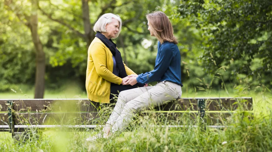 Ein Mutter und ihre erwachsene Tochter sitzen gemeinsam auf einer Parkbank.