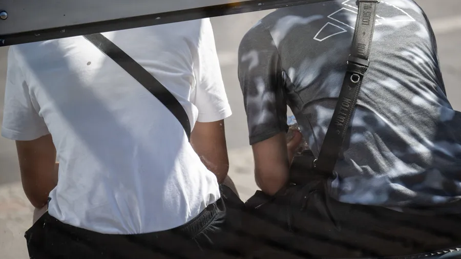 Jugendliche mit Umhängetaschen sitzen auf einer Bank. Macht sie das „Louis Vuitton“-Täschchen schon zu Talahons?