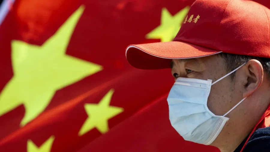 Ausbruchsort Wuhan: Ein freiwilliger Helfer mit Mundschutz und einer chinesischen Flagge im Hintergrund.