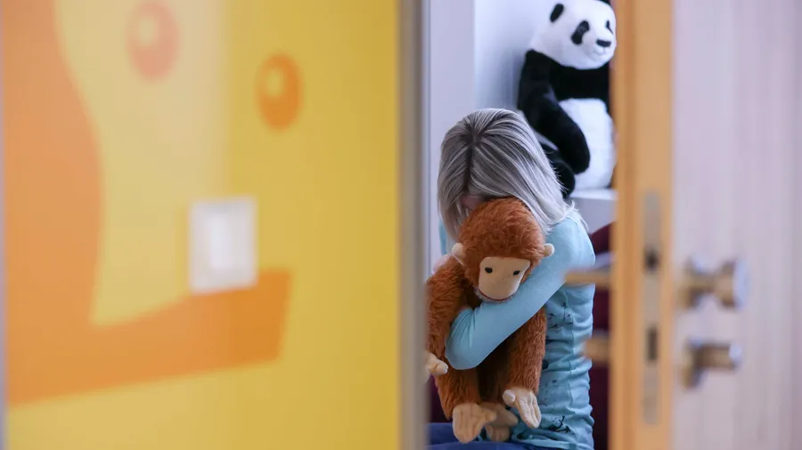 Eine junge Frau sitzt mit einem Kuscheltier im Arm in einem Raum des Childhood House, in dem Kinder und Jugendliche, die von Missbrauchs betroffen sind, vernommen werden können.