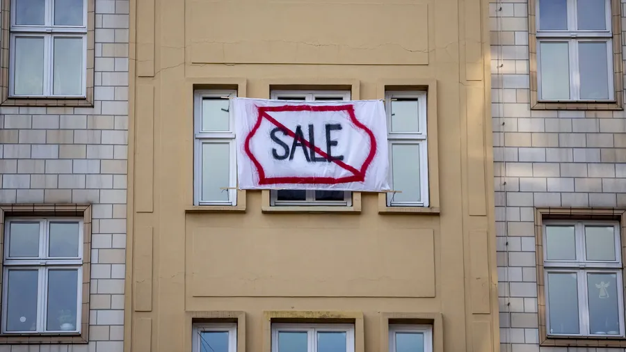 Ein Plakat gegen den Verkauf von Mietwohnungen an die Deutsche Wohnen SE hängt an einer Gebäudefassade in der Karl-Marx-Allee in Berlin.