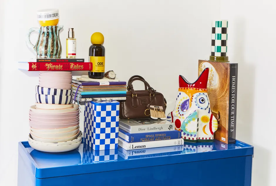 Von links nach rechts: Teller und Schalen von Ono Mao, „Pirate Tales“ von Robert E. and Jill P. May und „The Fire Next Time“ von James Baldwin und Steve Schapiro, beide aus dem Taschen-Verlag, gestreifte Kanne von Serax, darauf liegt eine Körpercreme von Sol de Janeiro, Rosen Pflegeöl von Dr. Hauschka, Aperitif von Ode, Uhr von Nomos Modell Orion Neomatik Doré, darunter Strümpfe von Falke, Notizhefte von Montblanc, die karierte Box ist von Hay, „The Gourmand’s Lemon“, „Small Stories Great Artists“ von Laurence Anholt und „Dior/Lindbergh“ ebenfalls alle bei Taschen erschienen, Handtasche von Miu Miu, bunte Vase von Serax Ottolenghi, „Homes For Our Time 3“ von Philip Jodidio (Taschen), Kerze von Hay