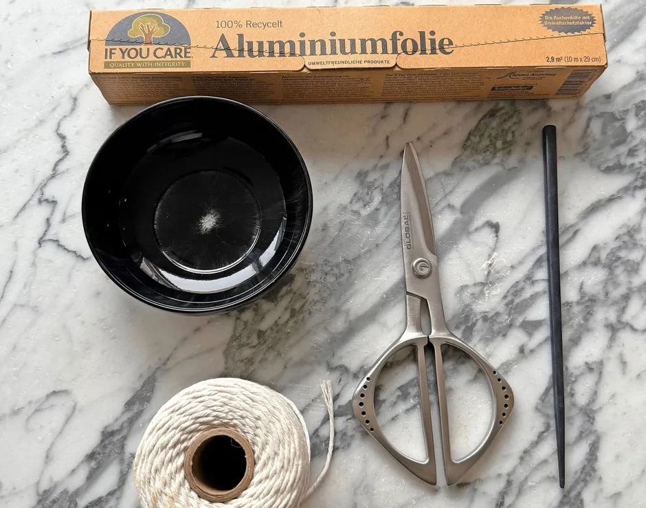 Man braucht: eine Schale, Alufolie, Schere, Schnur und Essstäbchen.
