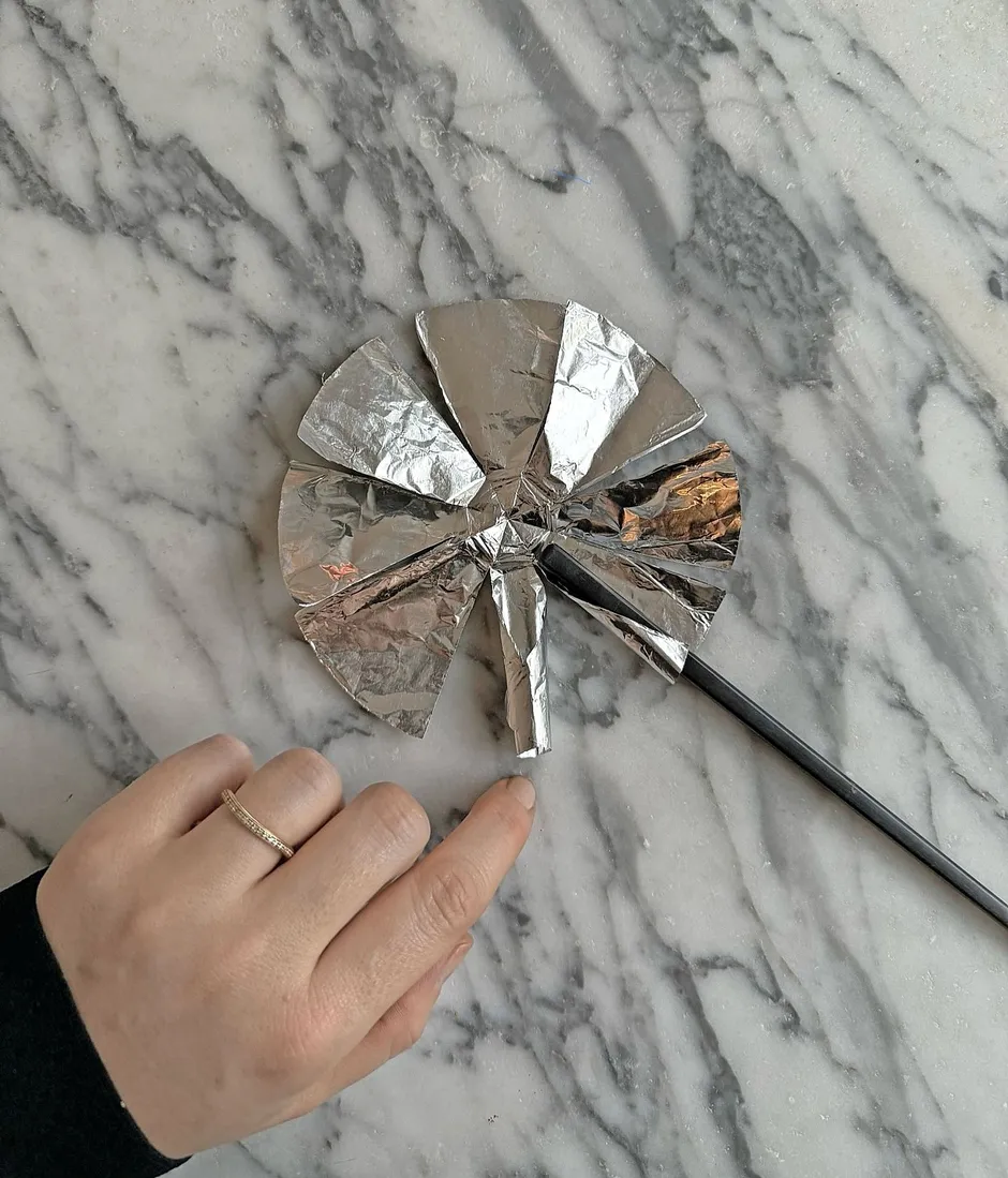Schritt 5: Stäbchen mit der breiteren Spitze an die Kante des inneren Kreises legen und links und rechts das Stäbchen in Folie einrollen. Stäbchen vorsichtig herausziehen und mit allen eingeschnittenen Dreiecken wiederholen. Enden der Röllchen mit zwei Fingern zusammendrücken.