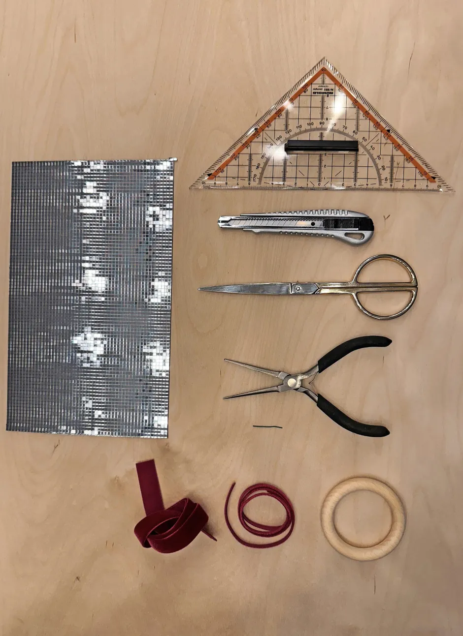 Man braucht: Cutter, Geodreieck oder Lineal, Zange, Samtbänder (10 mm und 5 mm breit), Draht (2 cm lang), selbstklebende Polystyrol-Spiegelfolie (Quadrate 5 mm), Holzring.