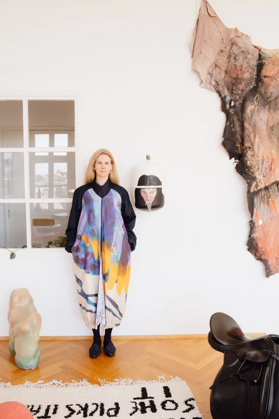 Linn Born in der Collection Born. Mantel: Sophia Süßmilch, Teppich: Josep Maynou, Kunst v. l. n. r. Oliver-Selim Boualam, Selma Selman, Raphaela Vogel, Ika Künzel