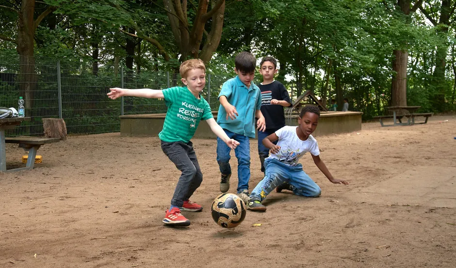 In einer Pause spielen Kinder Fußball im Hinterhof des Vorschulbereichs.