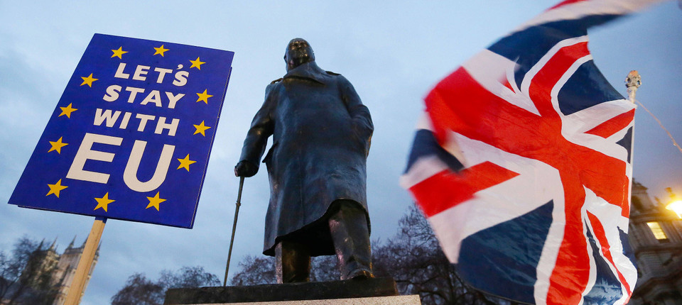 Brexit-Gegner halten ein Schild und eine Fahne bei einer Kundgebung vor einer Statue von Winston Churchill.