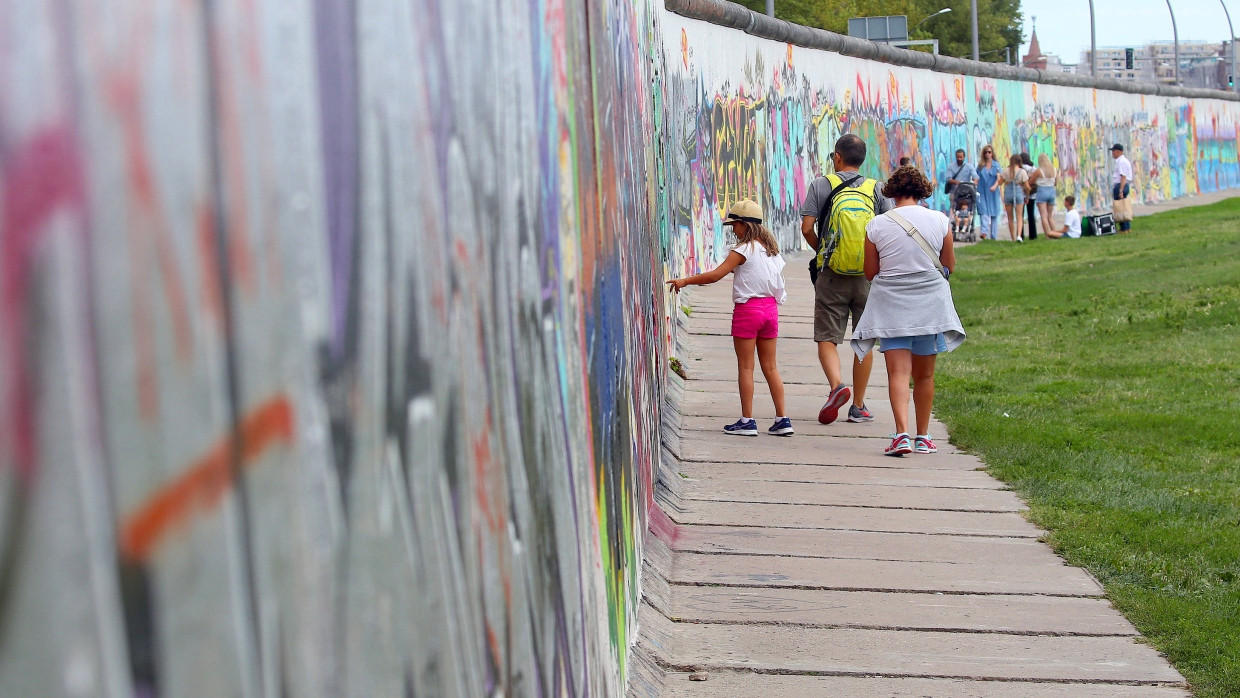 Am Gedenktag des Mauerbaus im Jahr 2019 gehen Menschen an einer Seite des längsten, noch erhaltenen Teilstücks der Berliner Mauer, der East Side Gallery, entlang.